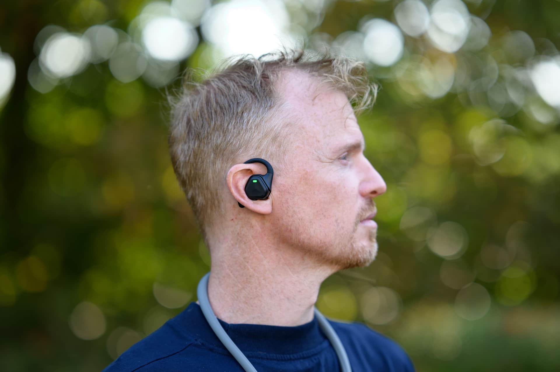 Close-up of the Insta360 POV Head Tracker accessory in Tim Coleman's ear, outdoors with dappled light in the background foliage