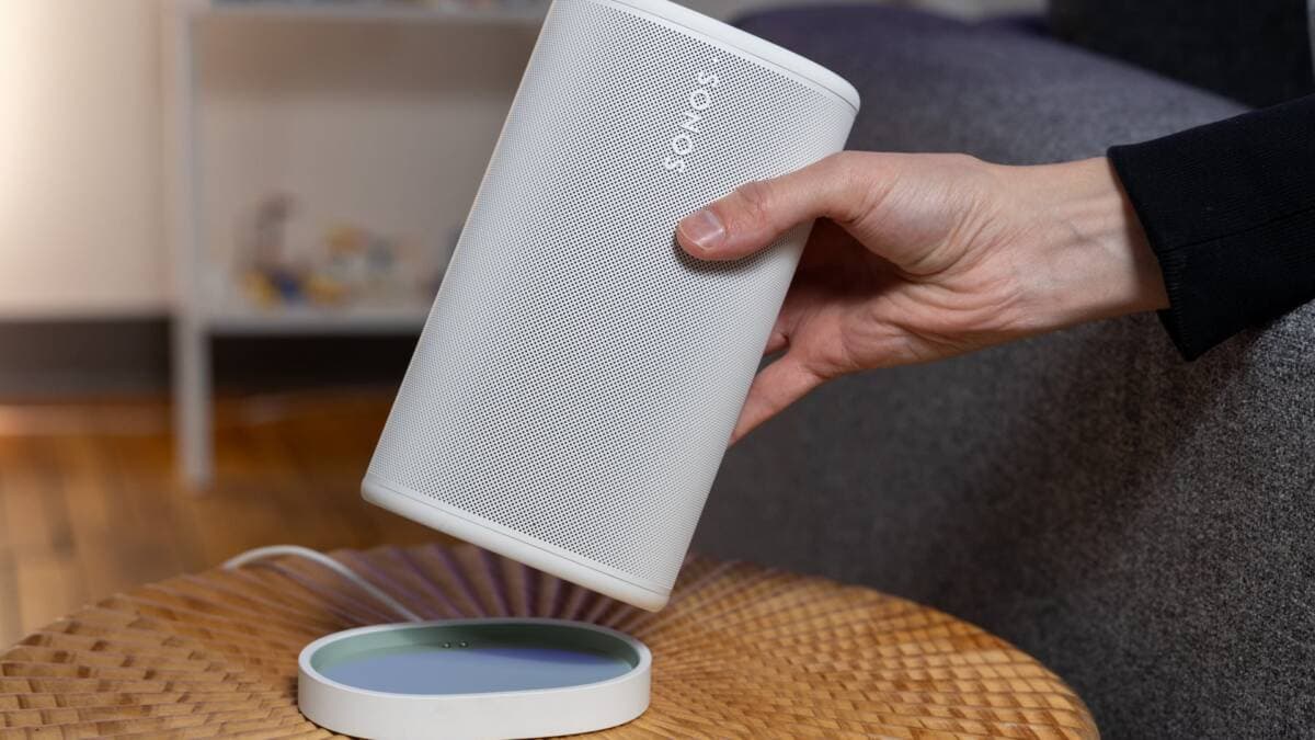 A white Sonos speaker held in a hand inside a home