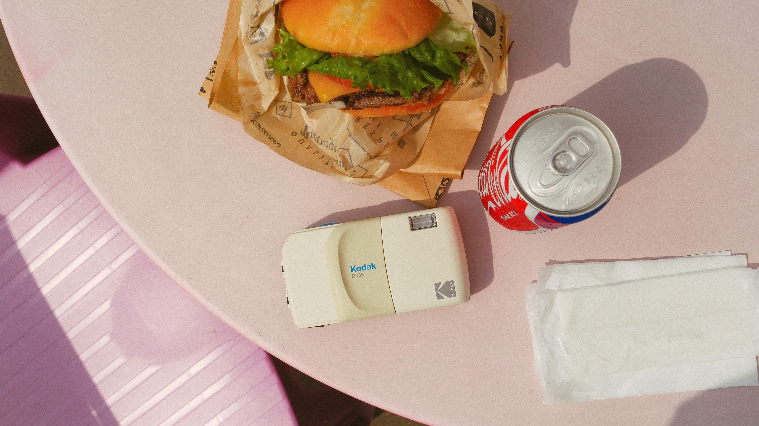 Photograph of the white Kodak EC35 film camera on a table beside a burger and a can of Coke