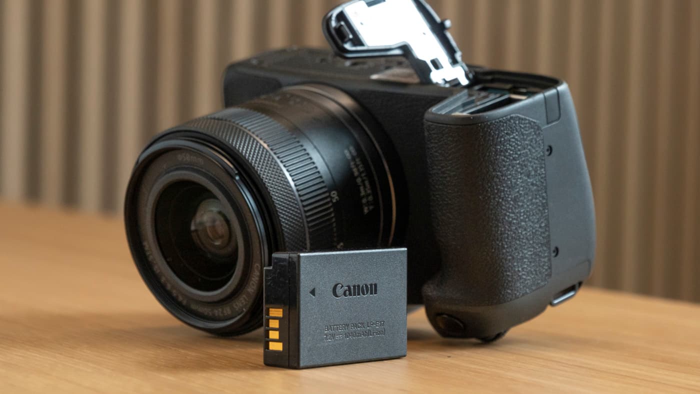 Canon EOS R8 camera on a table, upside down with its battery door open and battery beside it