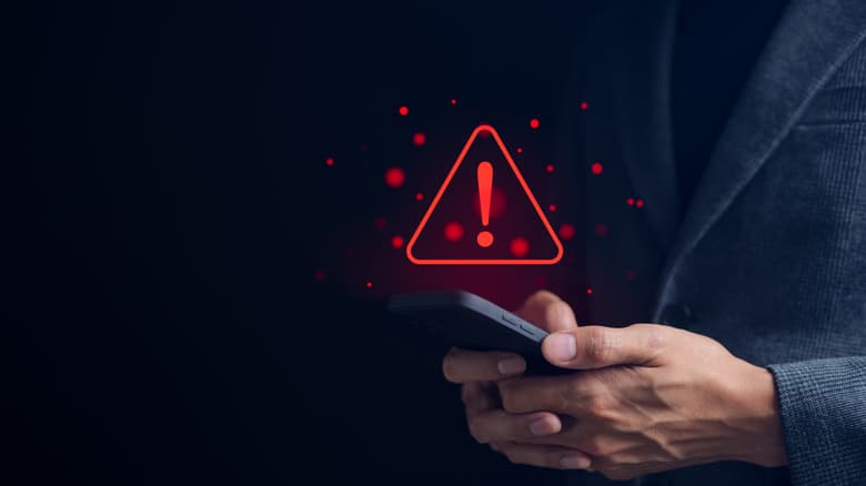 A person holding a smartphone with a triangular caution warning sign.