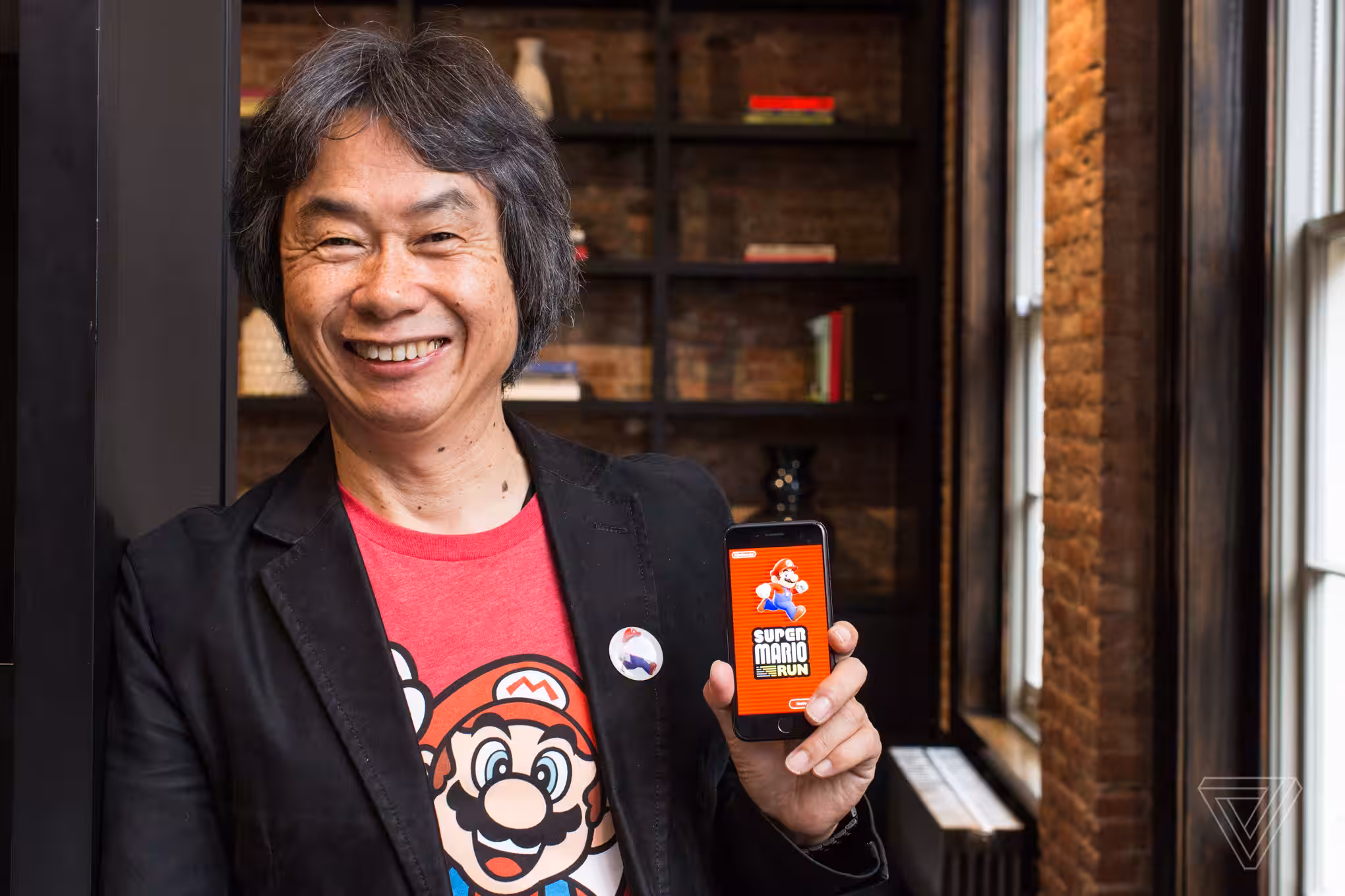 A photo of Shigeru Miyamoto holding up a phone playing Super Mario Run.