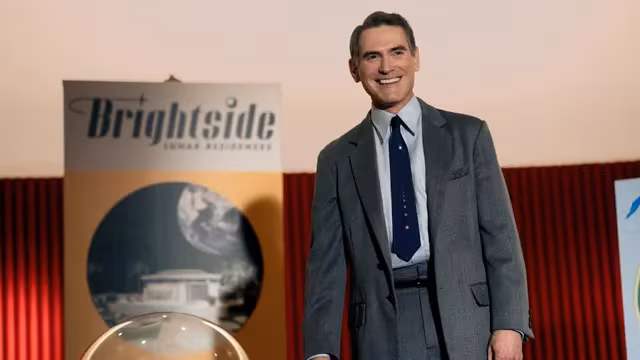 Man in suit in front of Brightside poster on Apple TV